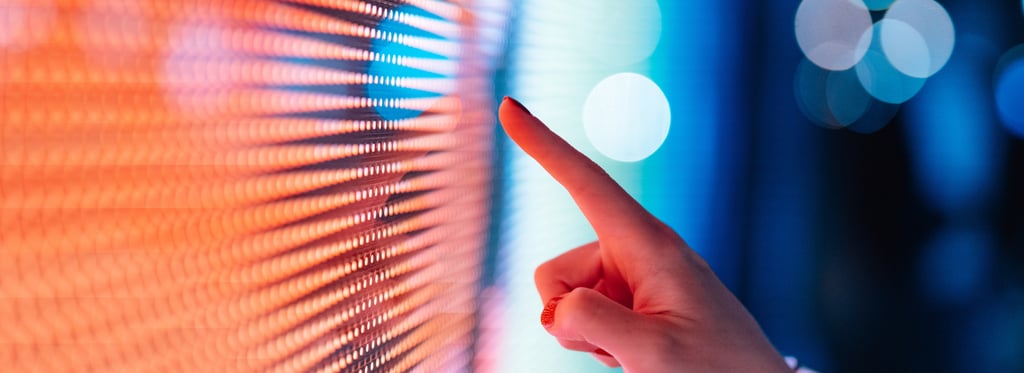 Hand pointing at a colourful LED screen with orange and blue pixels.